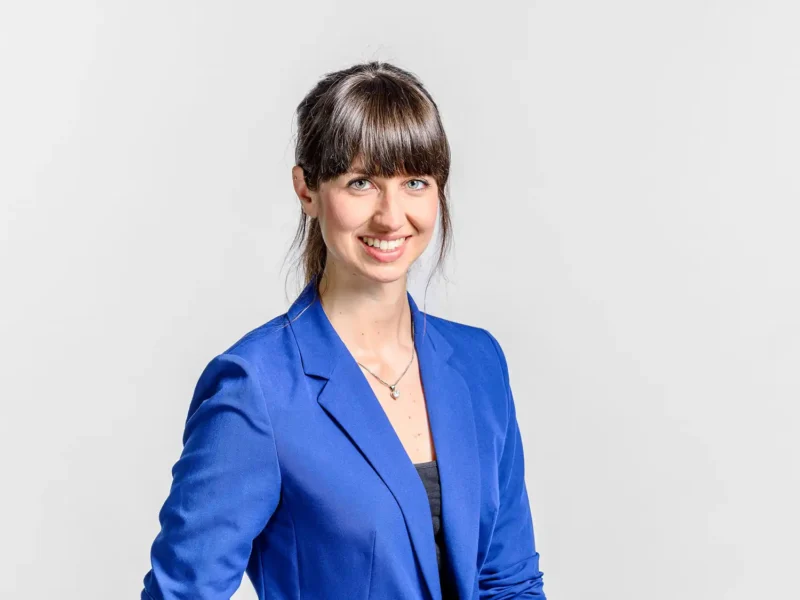 Businessportrait einer jungen Frau mit Pony und blauem Blazer vor hellem Hintergrund