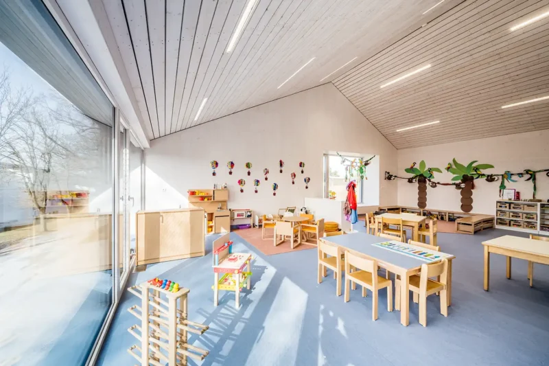 Architekturfotografie – Gruppenraum im Kindergarten Weitersfeld mit großer Glasfront und Holzmöbeln