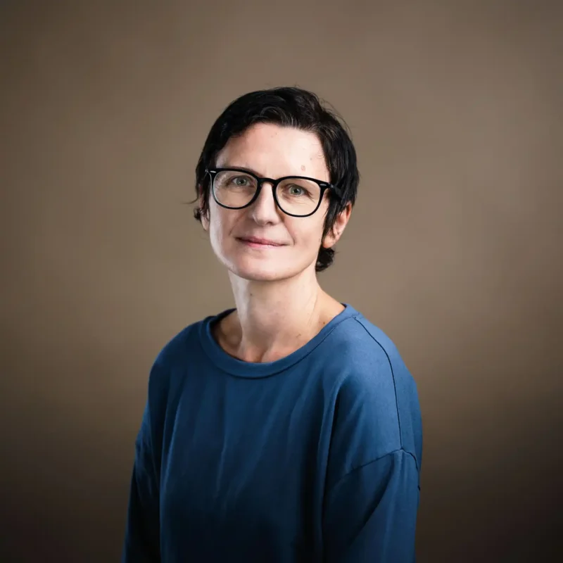 Businessportrait einer Frau mit kurzen dunklen Haaren, Brille und blauem Shirt, BOKU Wien