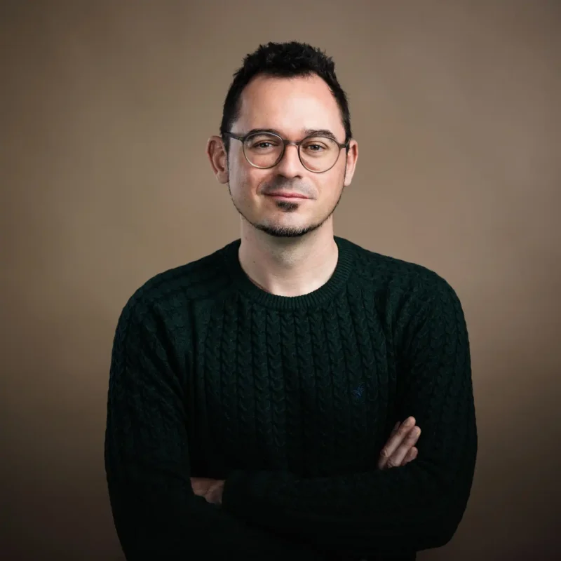 Businessportrait eines Mannes mit dunklem Haar, runder Brille und dunkelgrünem Strickpullover, BOKU Wien