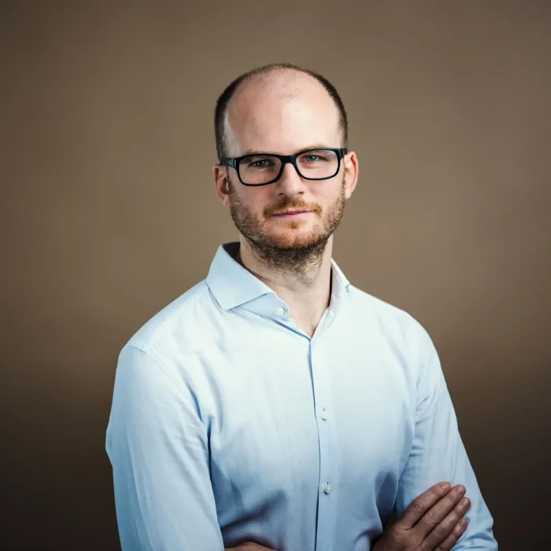 Businessportrait eines Mannes mit Glatze, Bart, schwarzer Brille und hellblauem Hemd, BOKU Wien