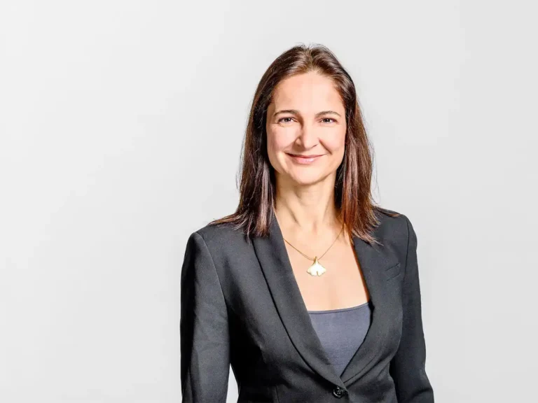 Businessportrait einer Frau mit langen braunen Haaren im dunklen Blazer vor hellem Hintergrund