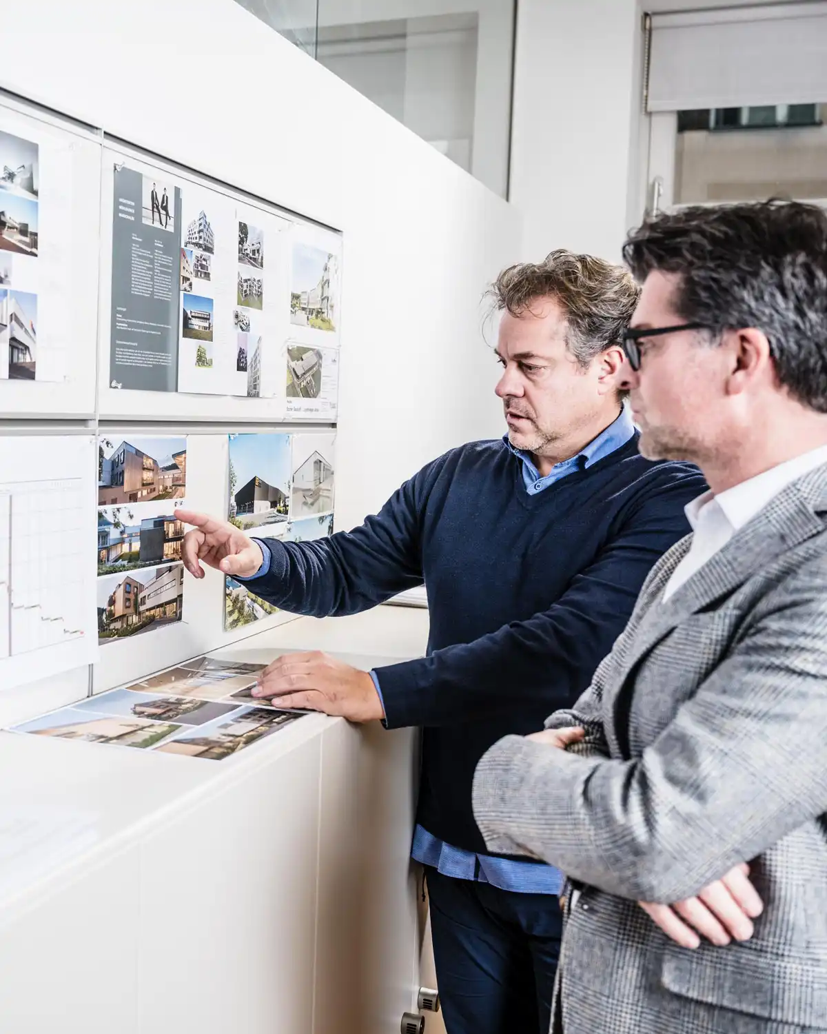 Architekten Mühlbacher und Marschalek bei der Projektbesprechung vor einer Pinnwand mit Architekturvisualisierungen in ihrem Wiener Büro