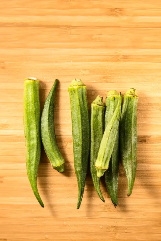 Food-Fotografie – Frische grüne Okraschoten auf hellem Holzbrett