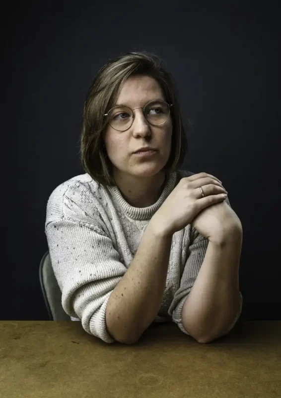 Portraitfotografie – Frau mit Brille und beigem Strickpullover vor dunklem Hintergrund, nachdenklicher Blick