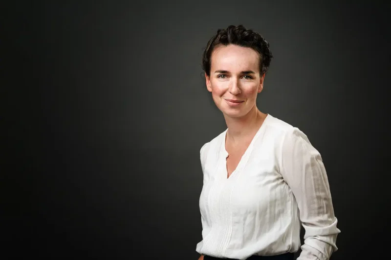 Portraitfotografie – Frau mit kurzen dunklen Haaren in weißer Bluse vor dunklem Hintergrund