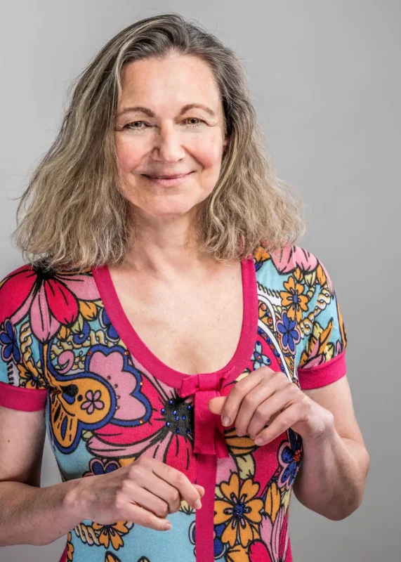 Portraitfotografie – Frau mit grau-blondem Haar in buntem Blumenshirt vor hellem Hintergrund