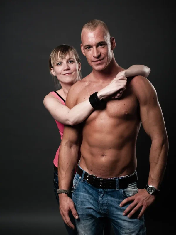 Portraitfotografie – Mann ohne Oberteil und Frau in rosa Top mit verschränkten Armen vor dunklem Hintergrund